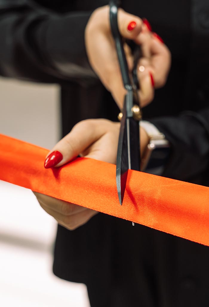 Woman holding ceremonial scissors and cutting ribbon for the grand opening of a local business.